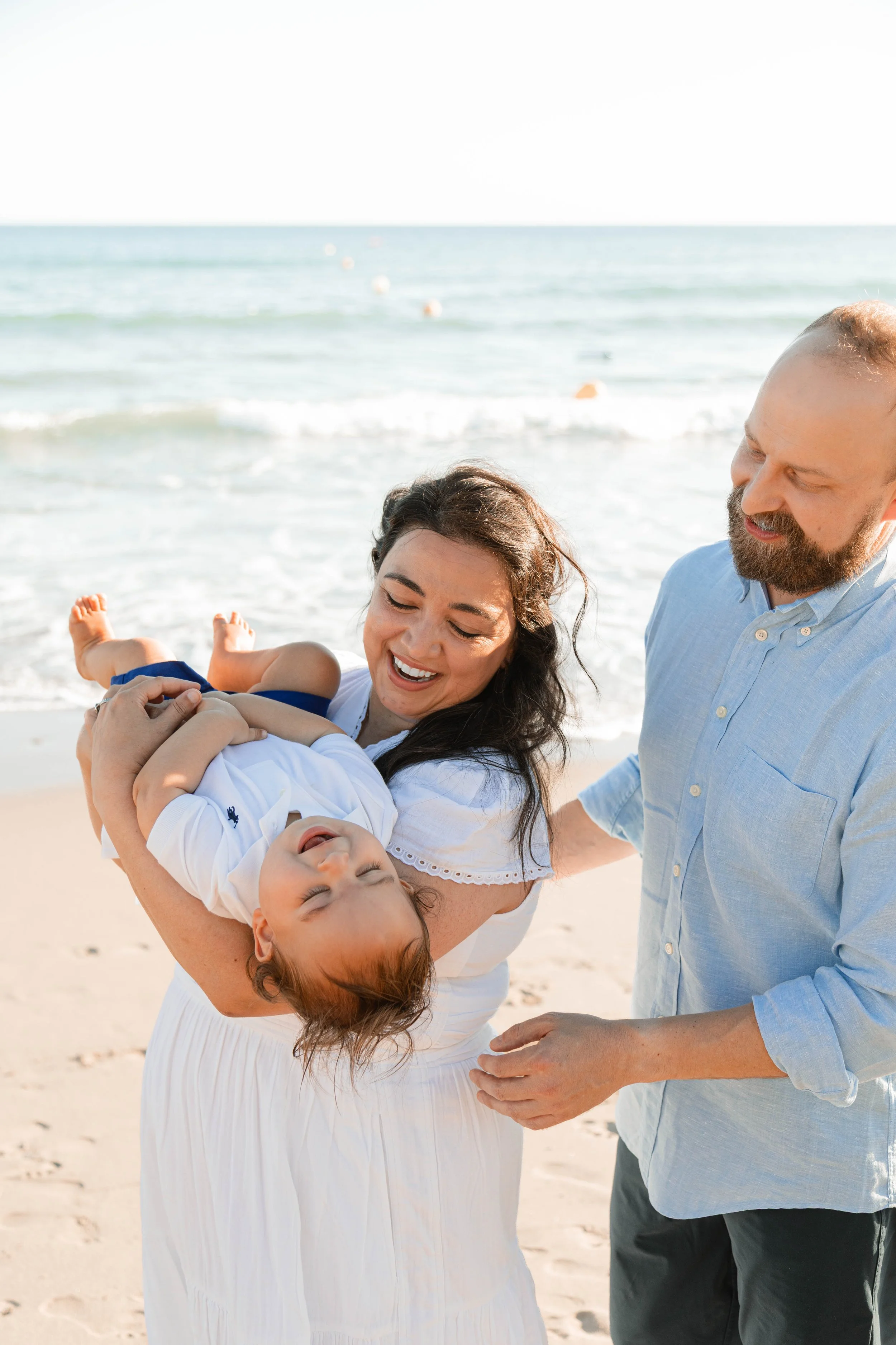 A happy family enjoying a day at the beach, with a woman holding a child and a man standing beside them.