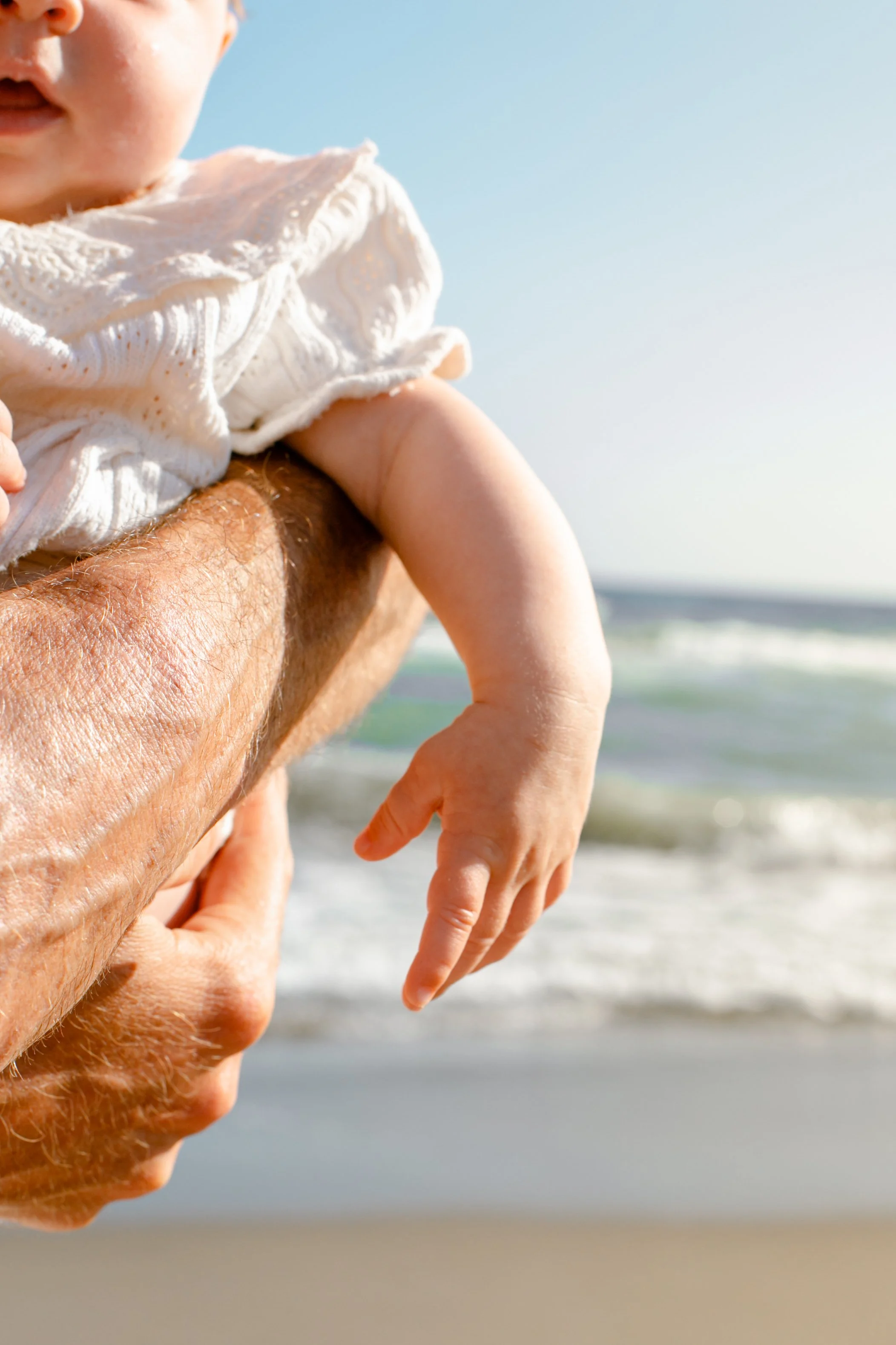 Person holding a small child at the beach with ocean and sky in the background.