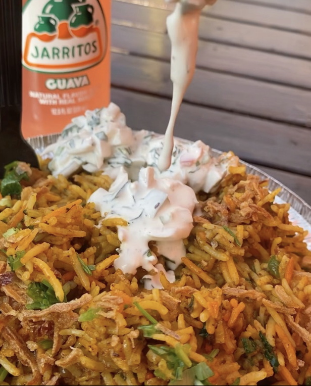 Close-up of Mexican rice with shredded meat, topped with sour cream and chopped herbs, served with a bottle of Jarritos guava soda in the background.