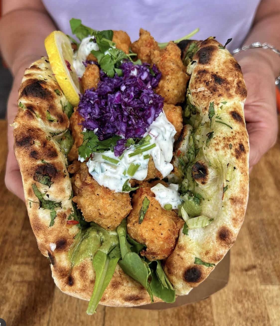 Fried chicken in a pita bread with purple cabbage, green herbs, lemon wedge, and white sauce.