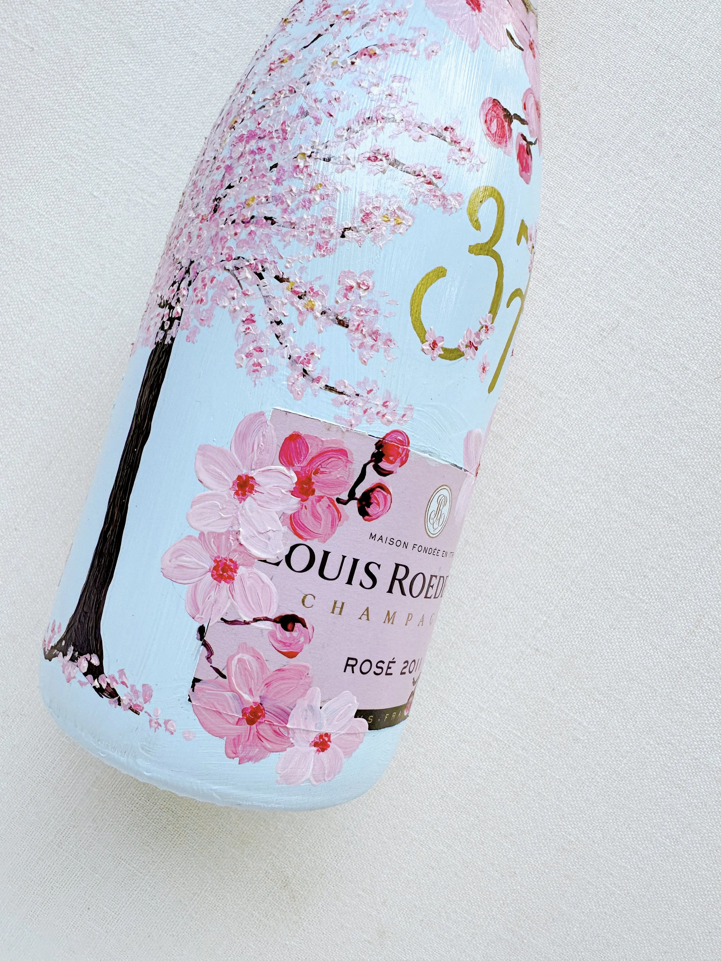 A close-up of a Louis Roederer Champagne bottle with a pink cherry blossom design on the label and a cherry blossom tree illustration on the bottle itself