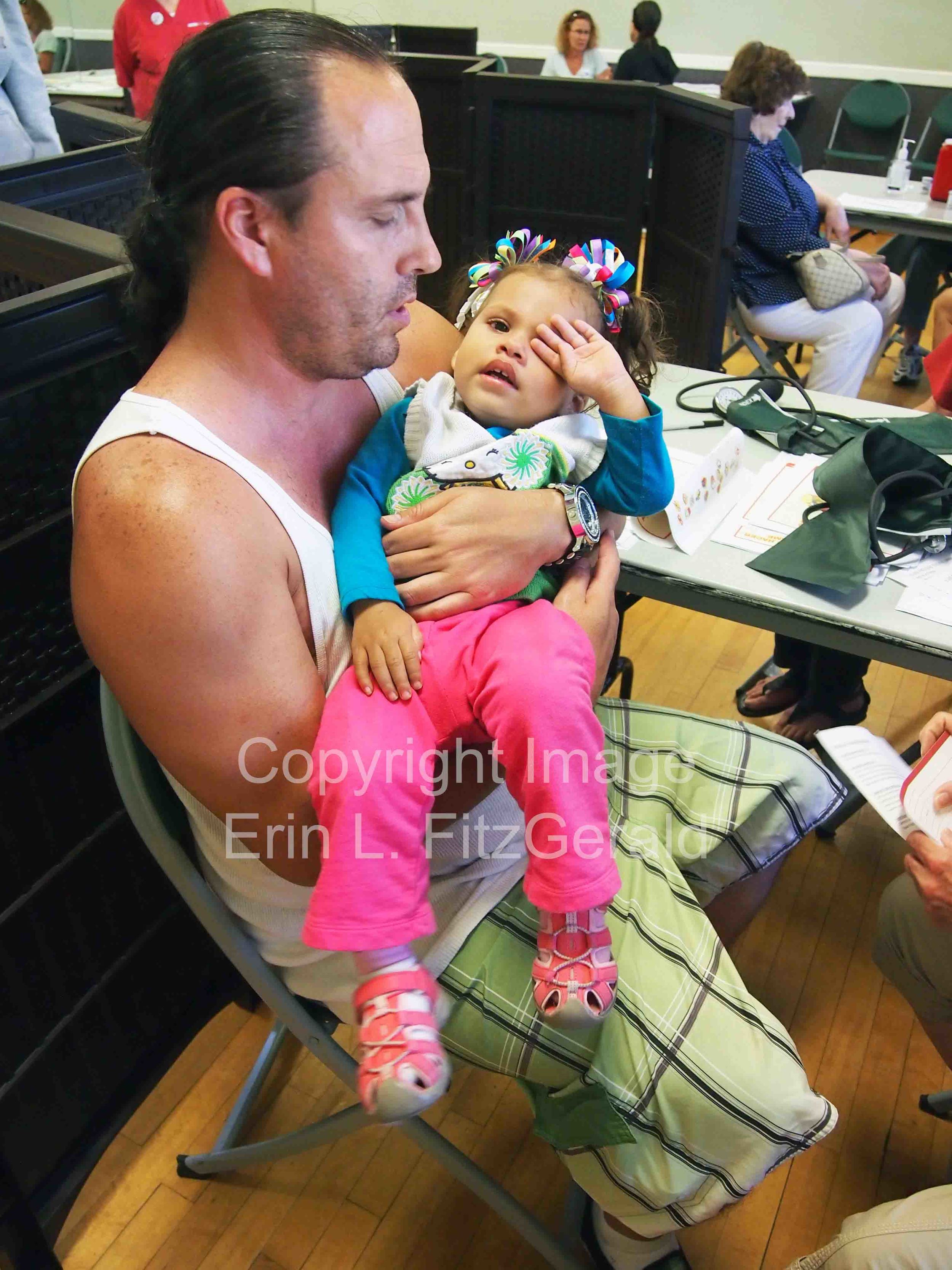   An man holds his daughter during health screenings during CNA's Medicare-for-All bus tour.&nbsp;  