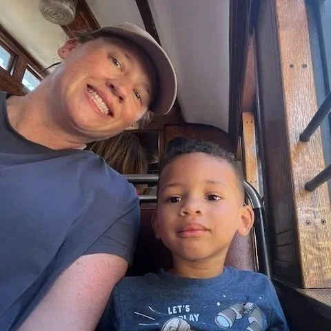 A man and a young boy sitting together inside a vehicle, smiling at the camera.