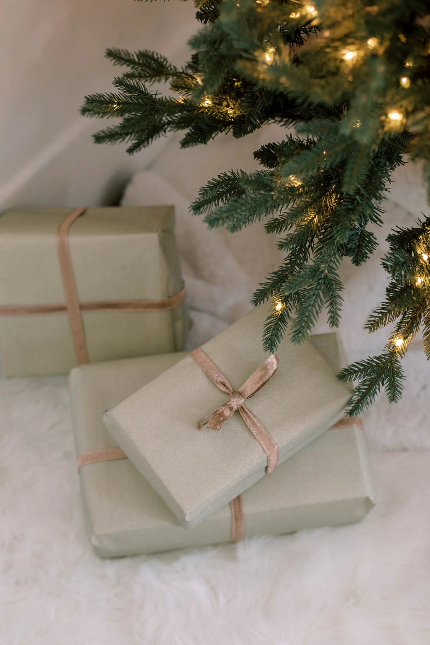 Decorated Christmas tree with illuminated lights and wrapped presents underneath, on a soft white furry surface.