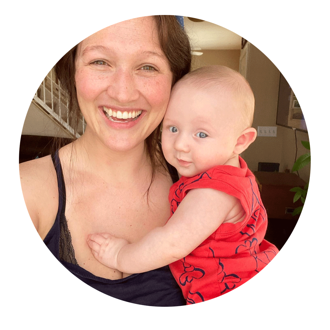 A woman with a big smile holding a baby with blue eyes, both indoors.