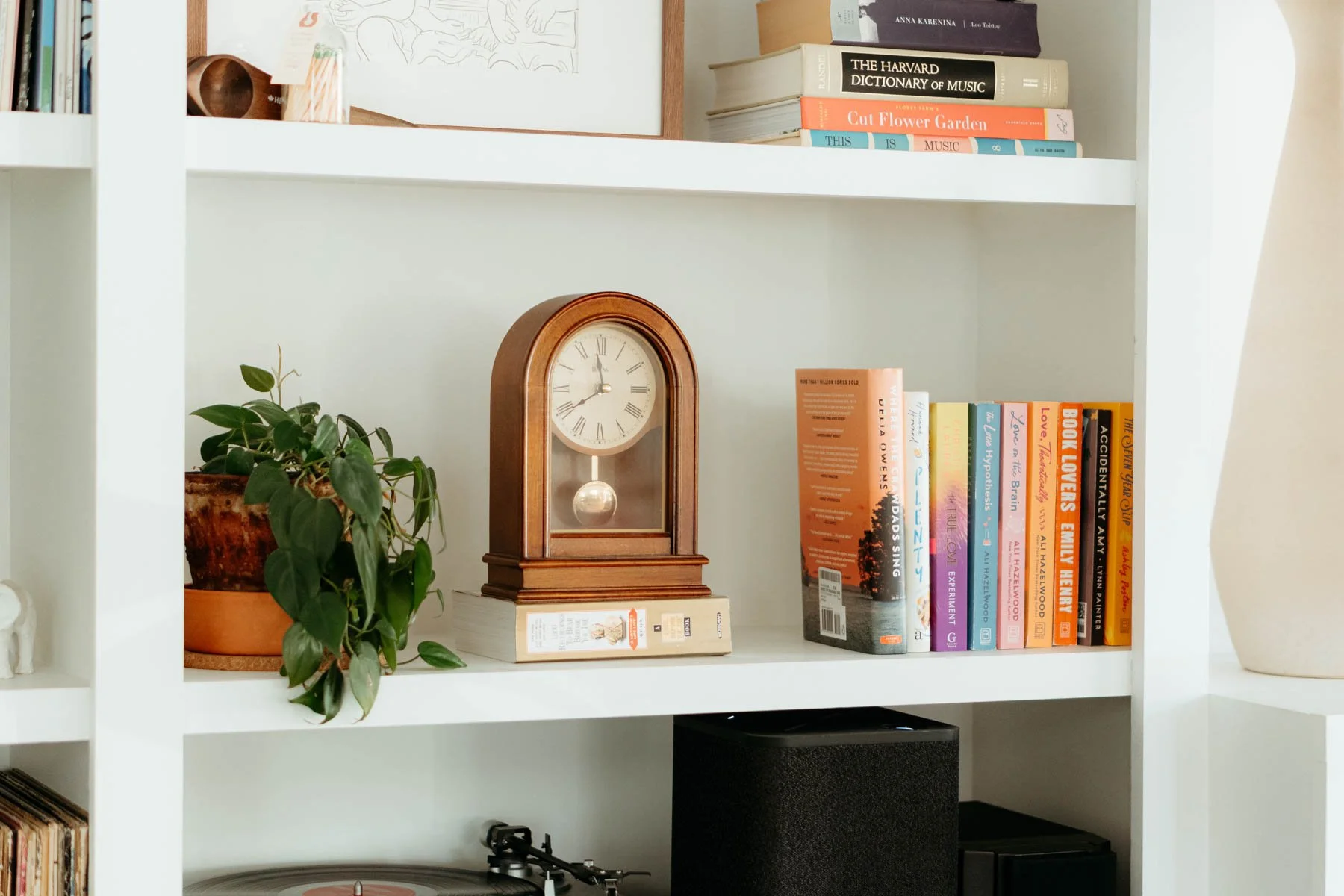 Bookshelf with a potted plant, a vintage clock, and various books on music, literature, and gardening.