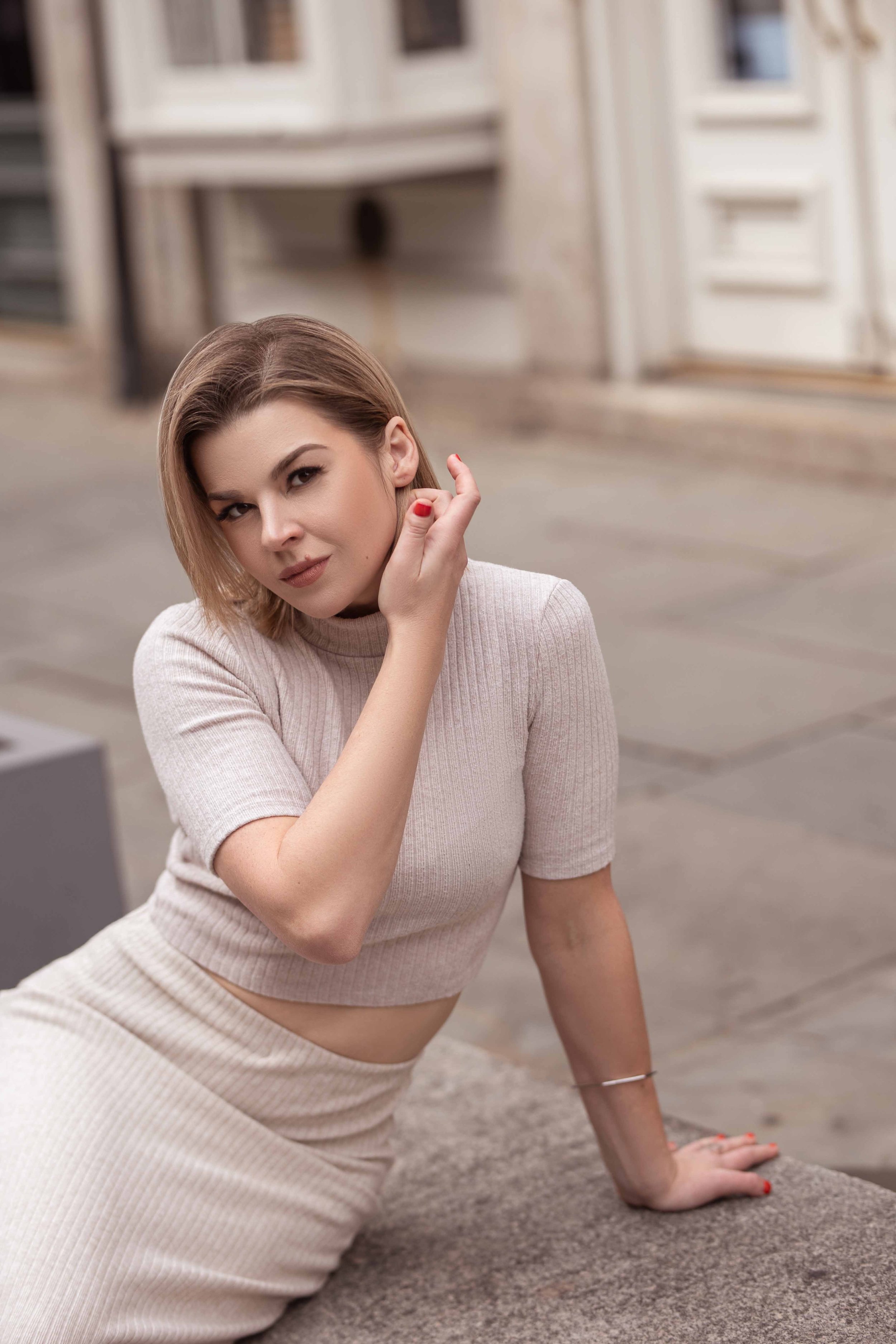 A young female business owner wearing casual - chic outfit in an urban setting, looking at the camera with a slight smile, modern headshot for branding.