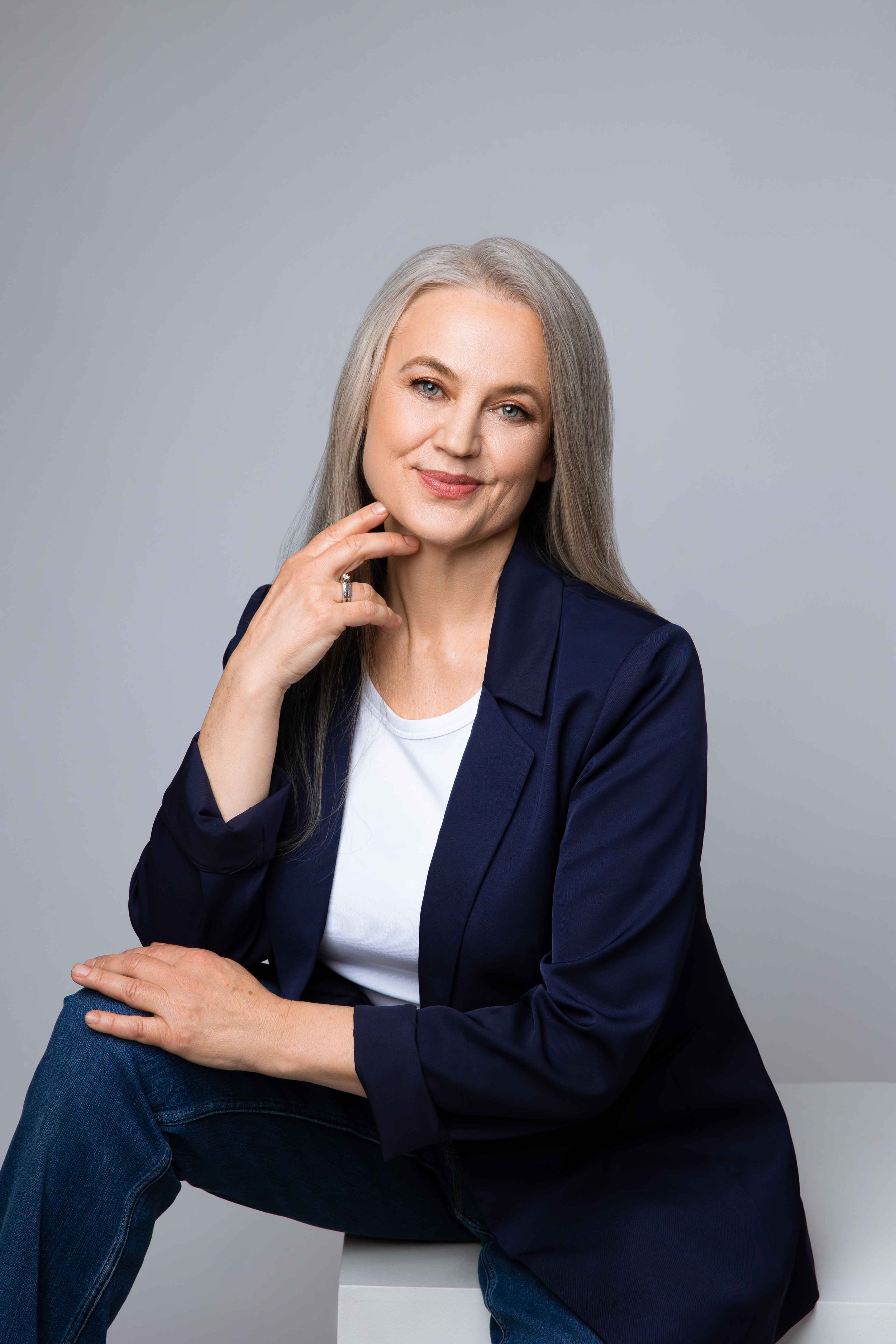 A mature female entrepreneur sitting relaxed with one hand touching her face during studio branding session.