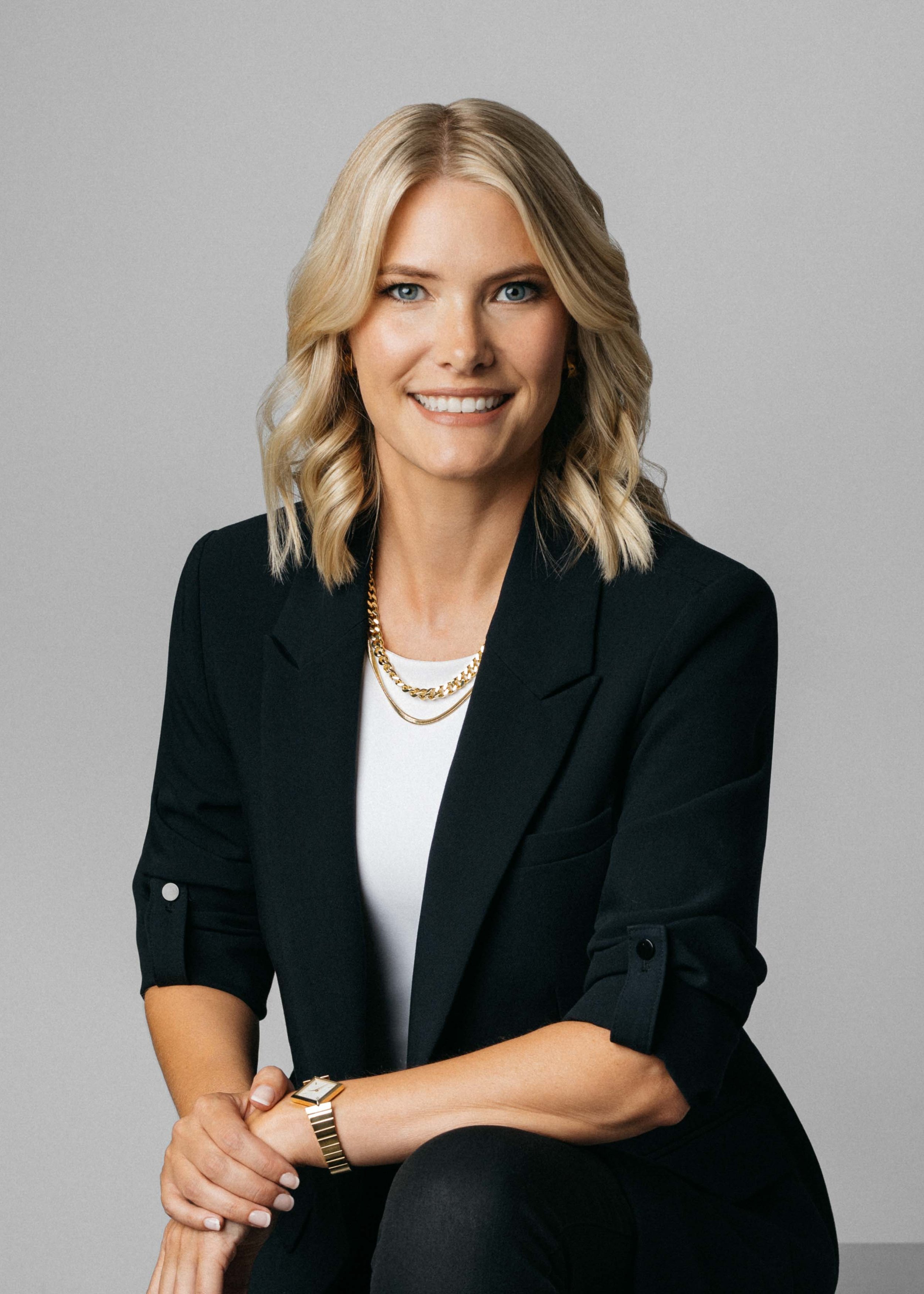 A woman in professional attire sitting confidently and relaxed, smiling in the camera during portrait session in the studio.