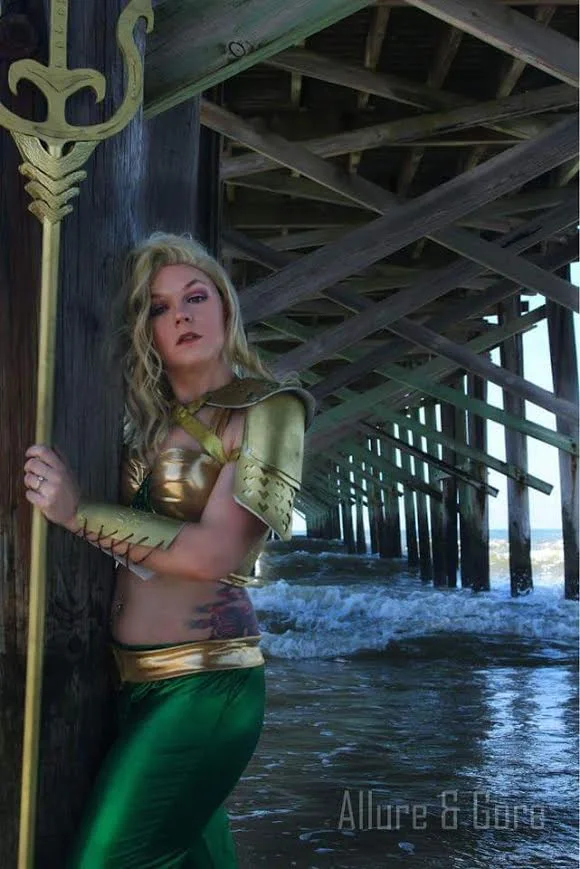 Aquaman 1.0- DC 100% head to toe made by me. My first armor pieces. The pauldrons are made of sintra plastic and foam. Those bracers in the picture were updated with much sturdier ones (and nicer pattern as well!). The top is a bra frankensteined into a crop top, it was resewn with the gold and green. then the green was covered in individually placed beetle wings. The pants were my first pair I ever made. The belt was made with the same gold as the top. And I added the logo which was made out of foam. The shoes were covered with the same green fabric as the pants. And the trident is PVC pipe, foam and the top piece is plywood (my husband cut out my design because I'm accident prone). I was on the phone with my brother (who is a police officer) and I was asking him who I should cosplay as (this was about 4-5 months into cosplay) because I wanted to do something for him as a thank you for being my hero. He told me I wish you were a boy so you could be Aquaman and he laughed. I said welp I guess that means I'll genderbend Aquaman. And this is what came out of that conversation. Also found out our girl cat Chibi enjoys eating beetle wings, who knew?!? Currently the trident is broken (although it is kinda fixed) thanks to my turtle Cleo, who decided to knock it down when it was just him and it in an empty(LARGE) room. Yes, that's real life. Currently Aquaman 2.0 is in the queue. New Armor, new top, new belt, and new trident. Photo by Diva and Death (formerly Allure and Gore): www.facebook.com/diva.n.death