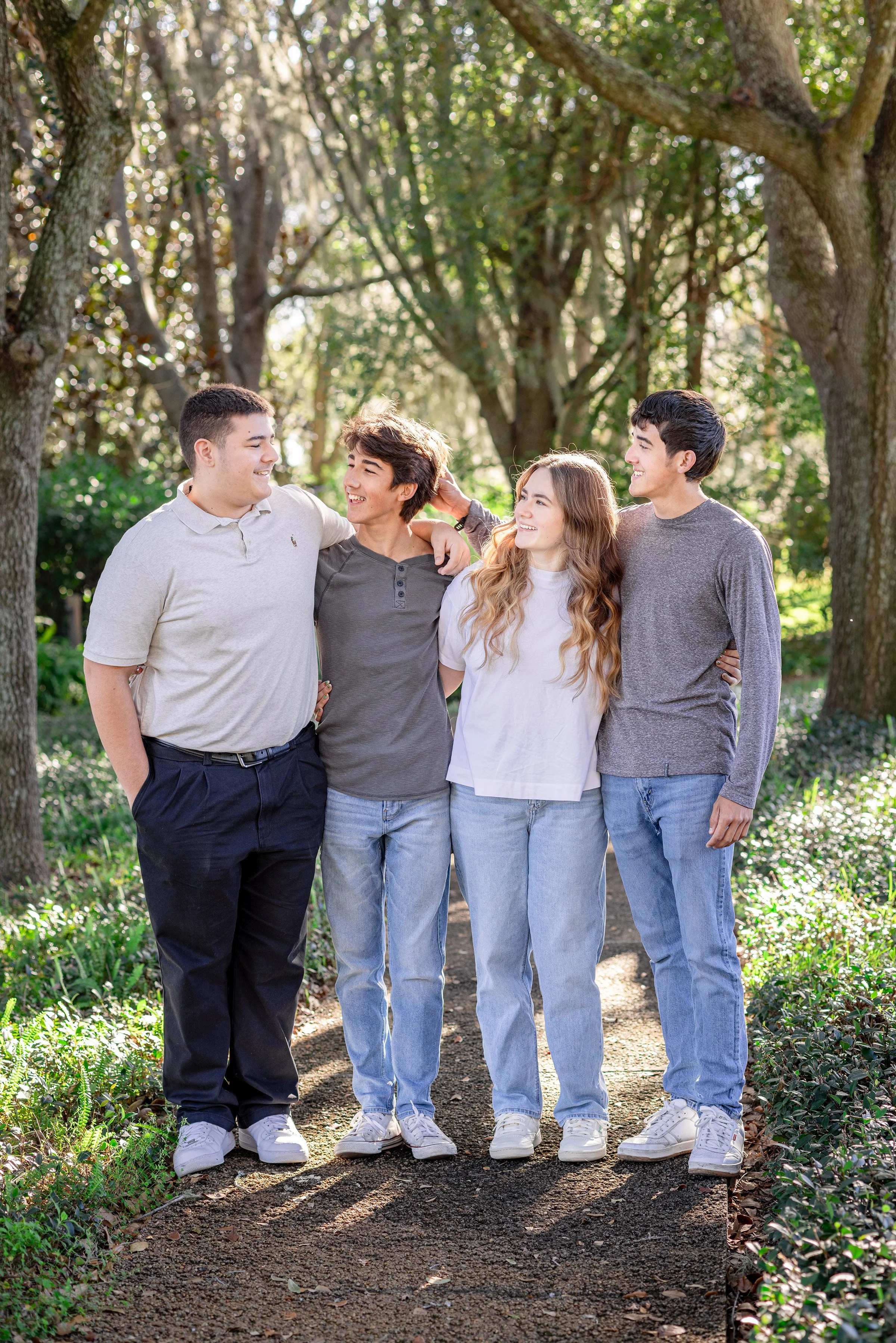 Four teenagers walking together on a wooded trail, smiling and enjoying each other's company in a park setting.