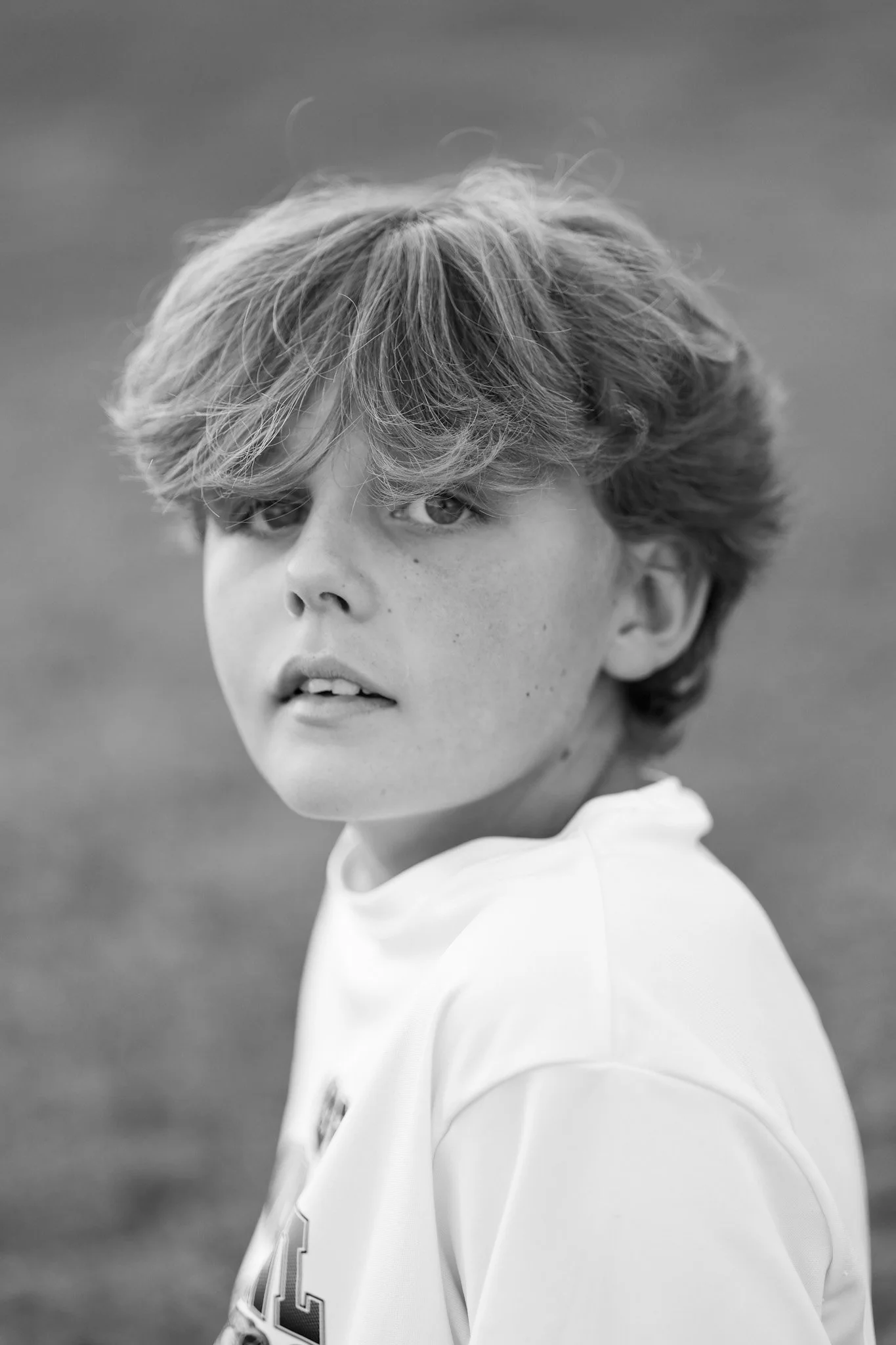 Black and white close-up portrait of a young person with wavy hair looking at the camera, wearing a sports jersey.