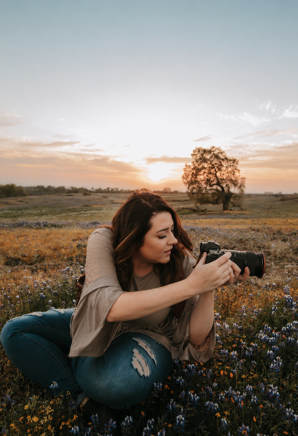 A woman sitting in a field of wildflowers at sunset, taking a photograph with a camera.
