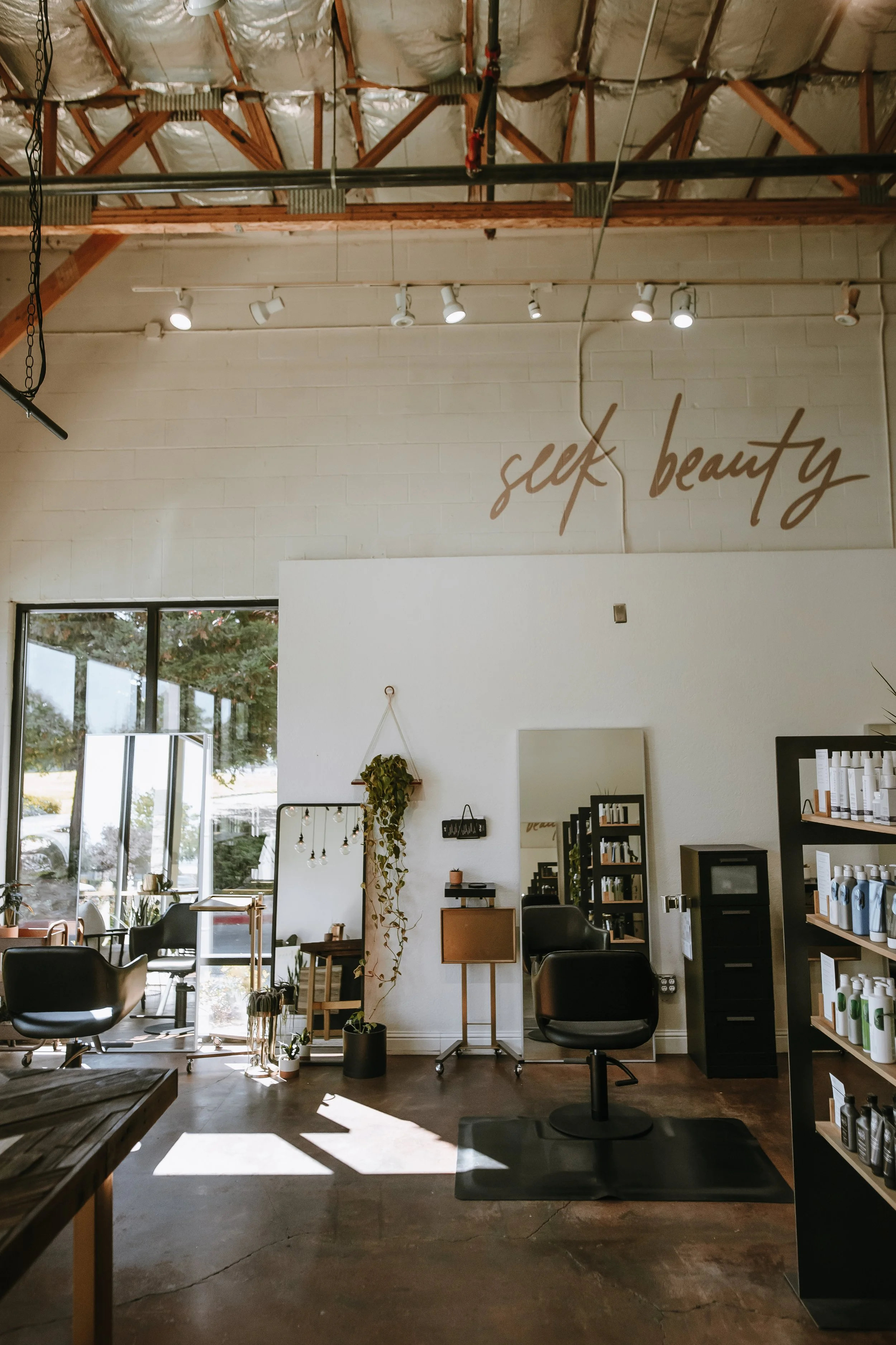 Interior of a hair salon with chairs, mirrors, and shelves of hair products. The wall has the words 'self beauty' written on it.