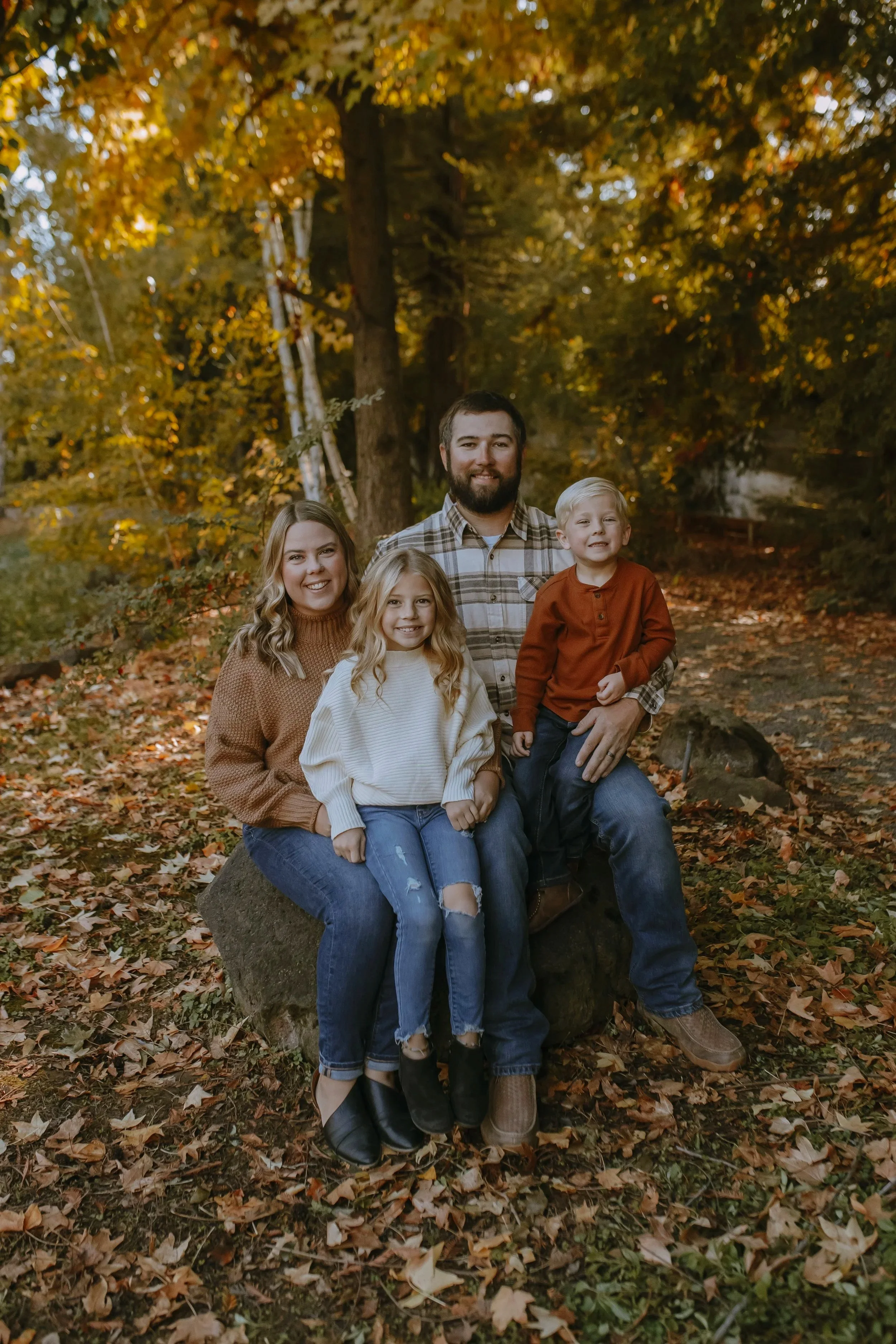 A family of five posing outdoors on autumn day, with trees and fall foliage in background.
