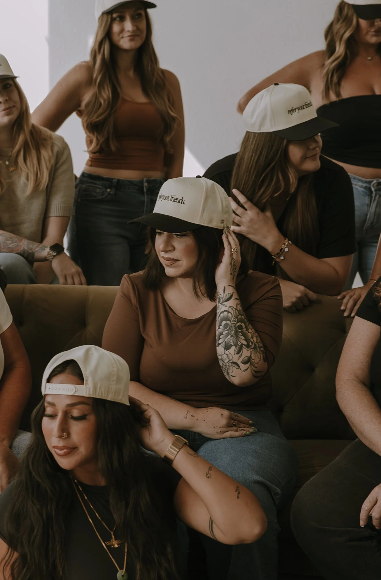 Group of young women wearing casual clothing, some with caps, sitting and standing indoors, smiling and relaxing.