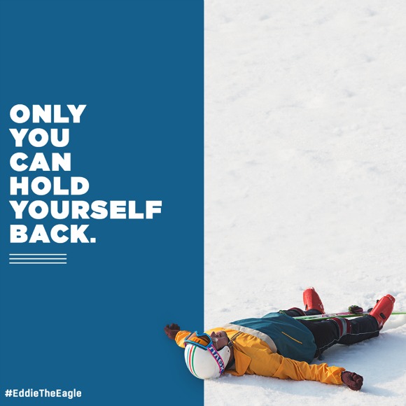 Photo Description: Left half of photo is blue with the words "ONLY YOU CAN HOLD YOURSELF BACK." In the bottom left reads #EddieTheEagle. The right half of the photo is of a snowy ground, a man lays at the bottom of the image wearing full ski gear, looking as if he is about to make a snow angel.