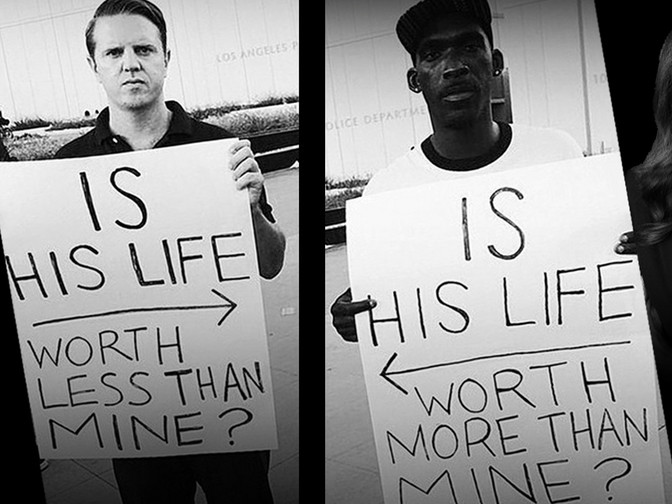 Photo Description: Two photographs, side-by-side. On the right is a dark-skinned man with a look that seems to say he is used to this. Serious, but almost bored. In his hands is a sign "IS HIS LIFE WORTH MORE THAN MINE?" On the sign, there is an arrow pointing to the man on the left. On the left is a light-skinned man with a look of anger and disgust. He looks like he wants to hit something. He also holds a sign "IS HIS LIFE WORTH LESS THAN MINE?" On the sign there is an arrow pointing to the right