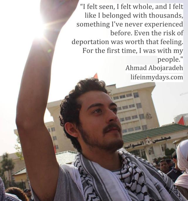 I stand in the sunlight, hands held high, with a Palestinian Keffiyeh around my neck. 