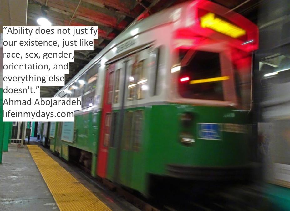 Photo Description: A green subway train in boston blazes past with a disabilities sticker blurred out in the front. 