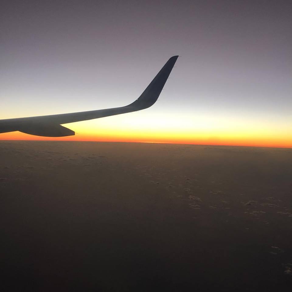 Photo Description: The sun sets below the right wing of a plane over Puerto Rico. 