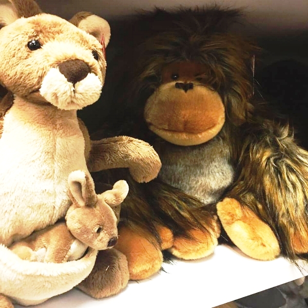 Picture Description: A family of stuffed animals, a Kangaroo with a baby in its pouch, and a monkey, smile at the camera from a white shelf. 