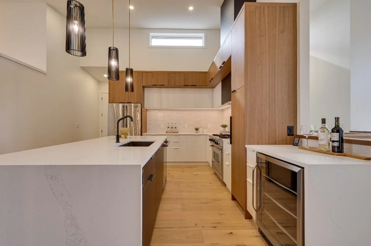 Modern kitchen with white and wood cabinetry, a large white island with a sink, and black pendant lights hanging from the ceiling.