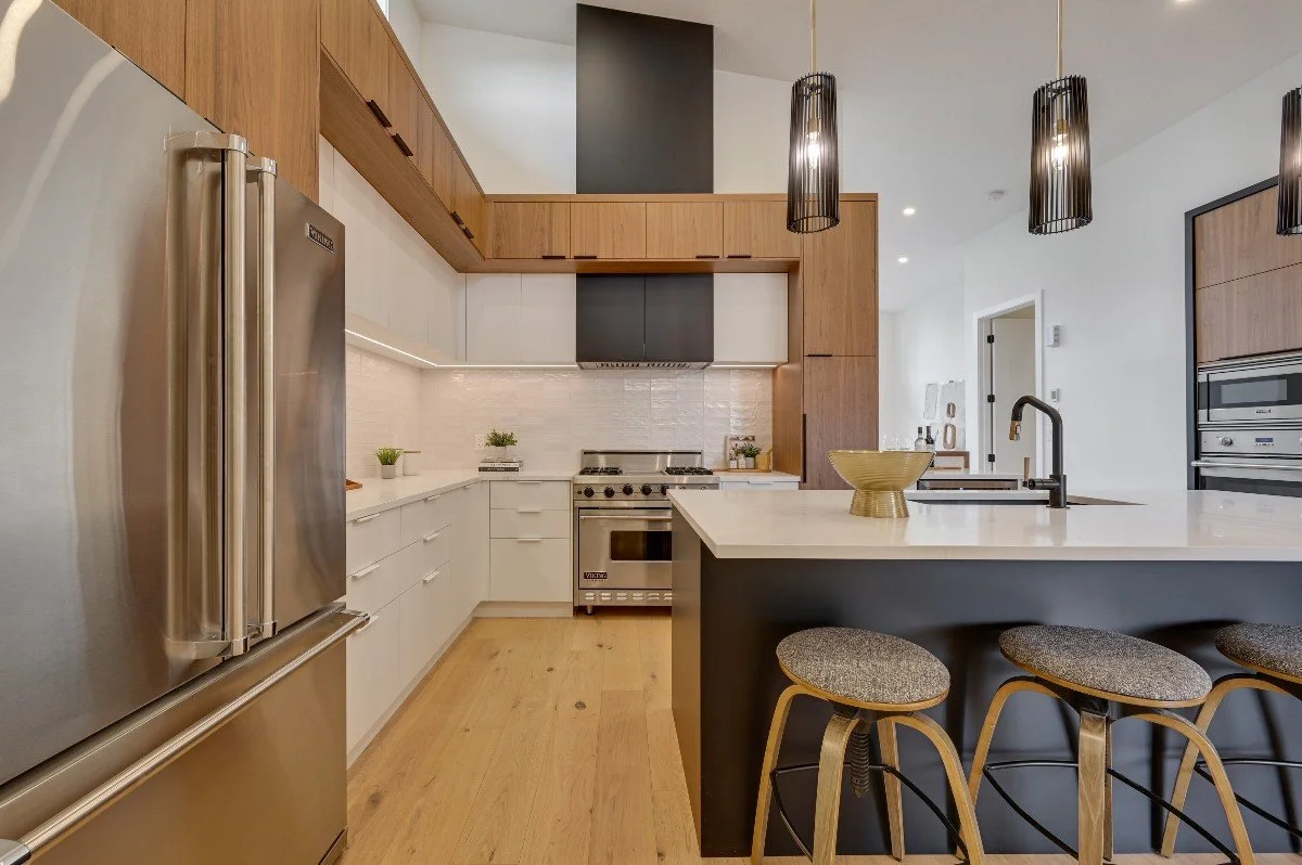 Modern kitchen with white and wood cabinetry, stainless steel appliances, pendant lights, and a white island with bar stools.