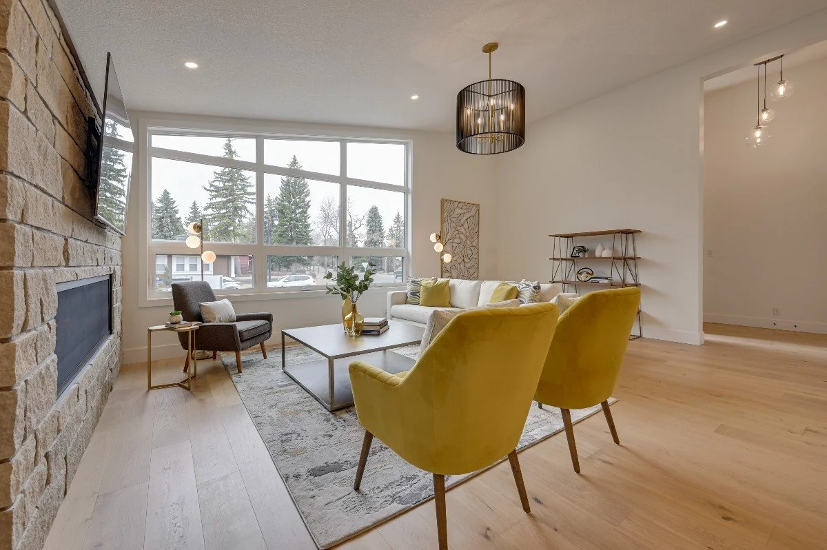 Modern living room with large windows, yellow and gray furniture, a stone fireplace, and wooden flooring.