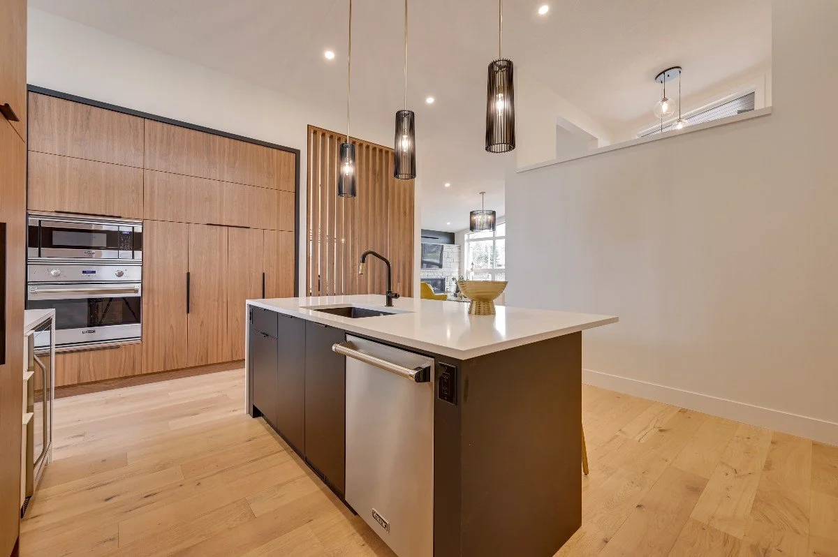 Modern kitchen with wooden cabinets, a black island with a built-in sink, pendant lighting, and a small refrigerator.