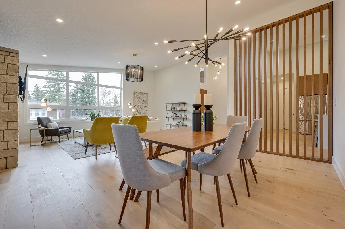 Open-concept living and dining area with large window, wooden flooring, modern chandelier, and a wooden slat partition.