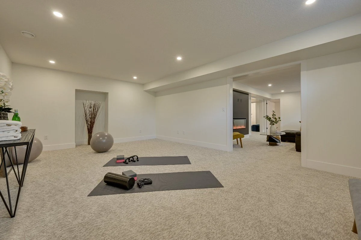 Basement with exercise mats, dumbbells, and stability balls, decorated with modern furniture, a fireplace, and minimal decor.