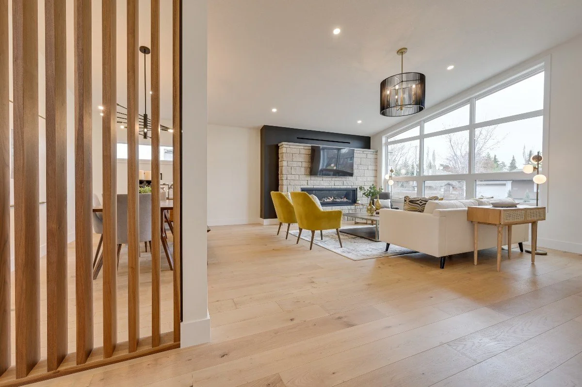 Bright living room with large window, white sofa, two yellow armchairs, a fireplace, and modern decor.