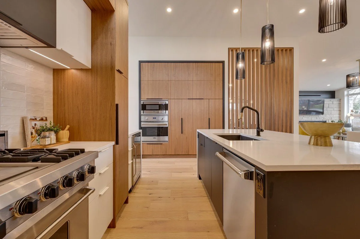 Modern kitchen with wooden cabinetry, white countertops, black pendant lights, stainless steel appliances, and a kitchen island with a sink.