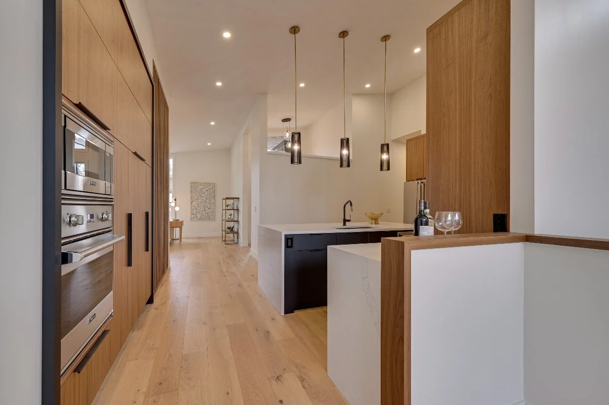 Modern kitchen with wooden cabinets, black and white countertops, pendant lights, and built-in appliances.