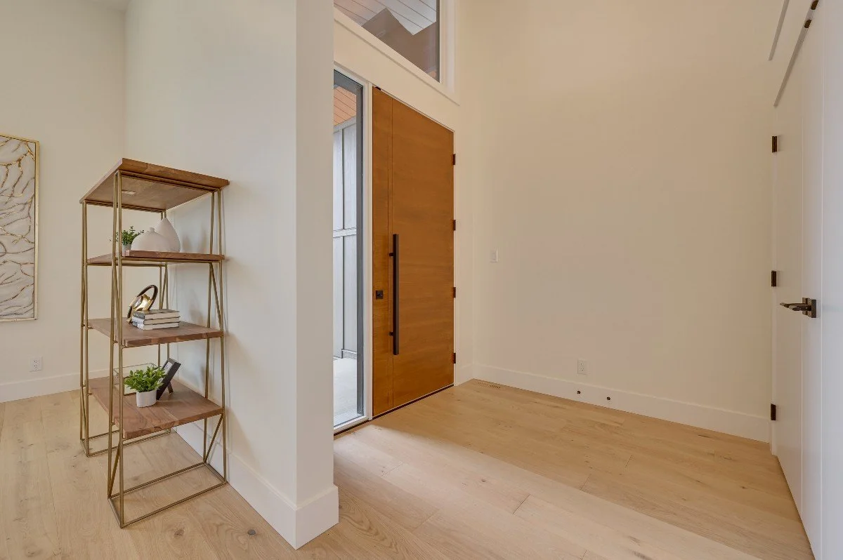 Entryway with wooden front door, small window, white walls, and light wood flooring.