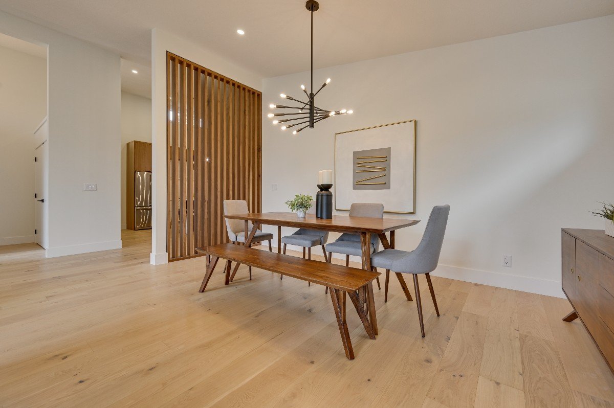 Contemporary dining room with wooden table, gray and beige chairs, modern chandelier, artwork on the wall, wooden floor, and a wooden room divider.