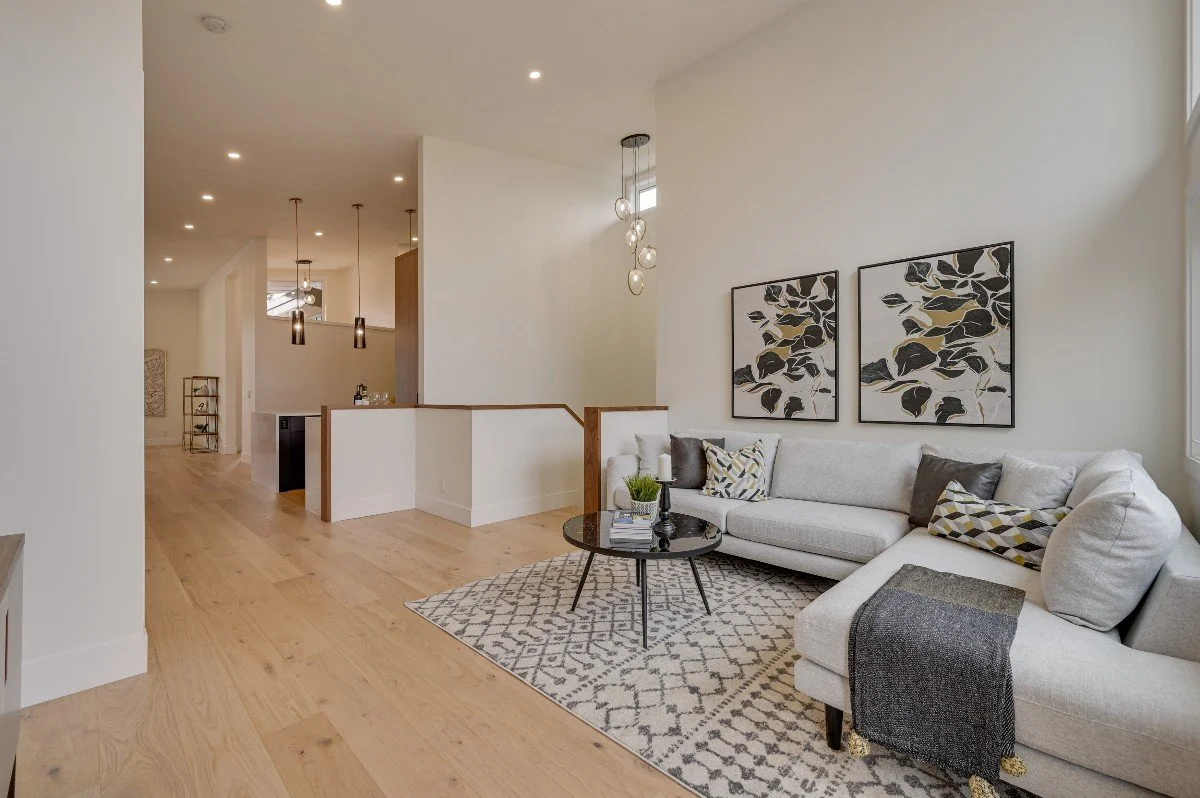 Living room with light-colored sectional sofa, black and patterned pillows, black coffee table, and wall art with abstract black and gold leaves.