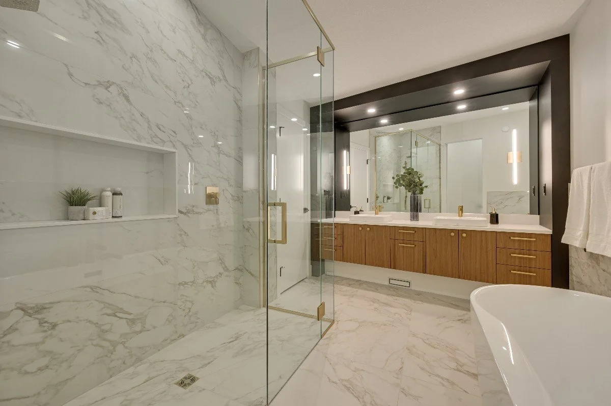 Modern bathroom with marble walls and floors, glass shower enclosure, large mirror, wooden vanity with two sinks, and a white bathtub.
