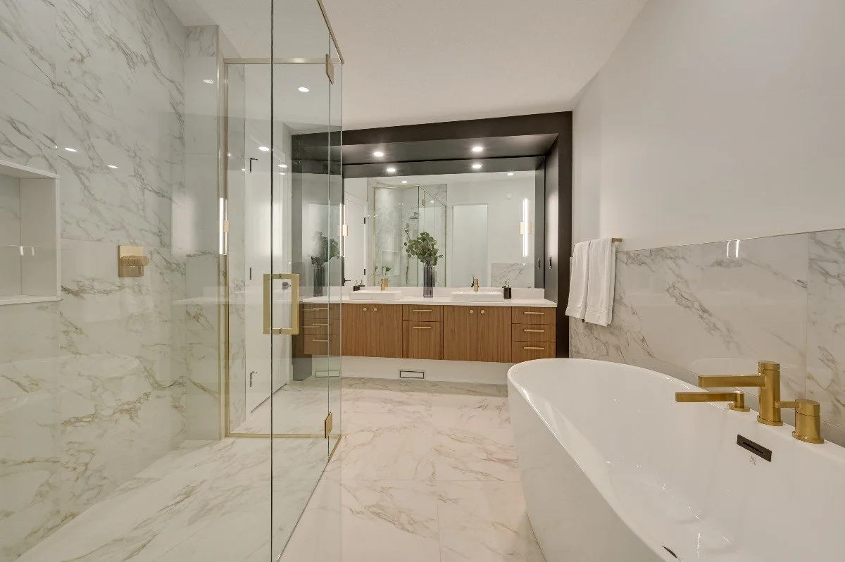 Modern bathroom featuring a large glass-enclosed shower, a freestanding bathtub with gold fixtures, a double vanity with a large mirror, and marble flooring and walls.