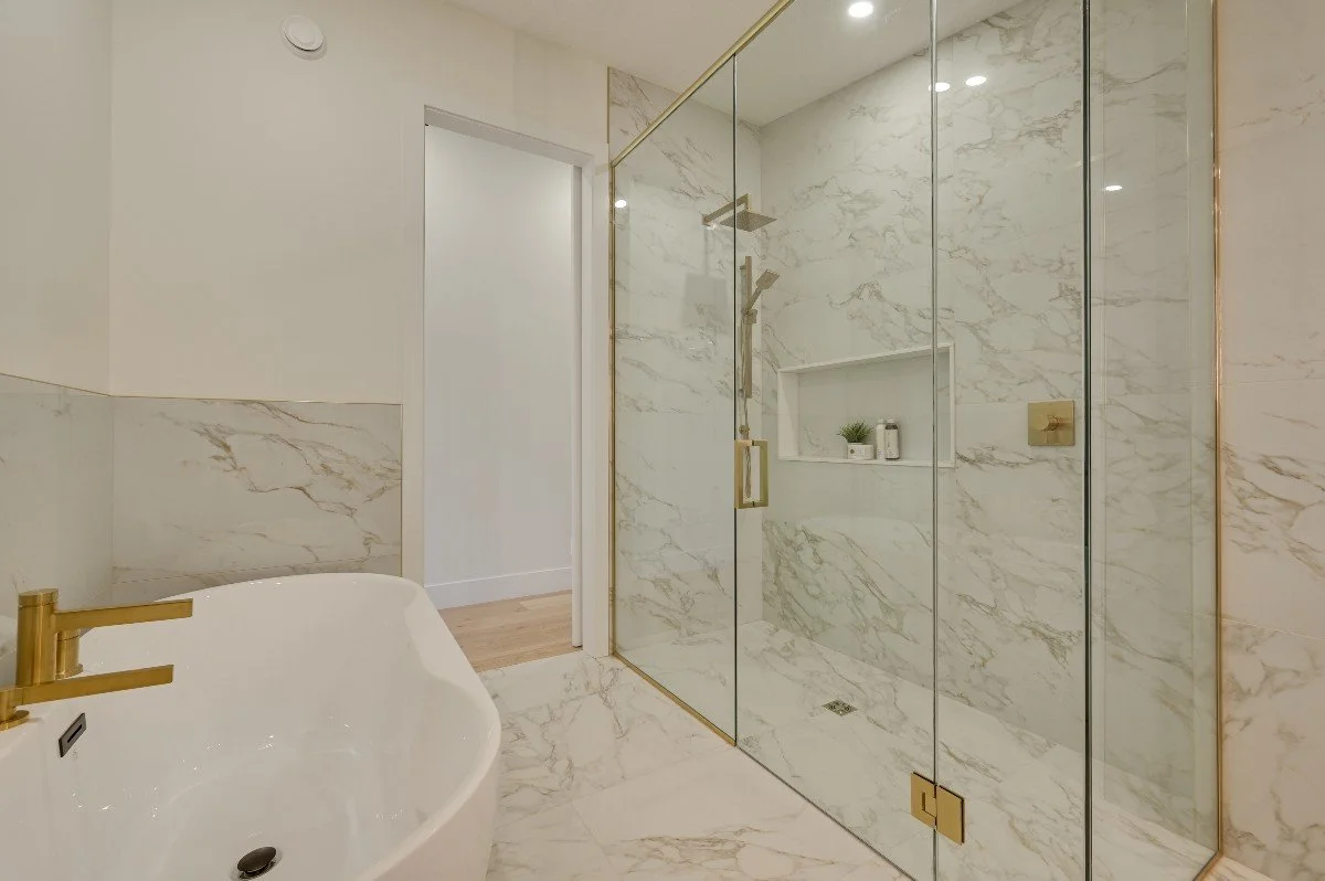 Modern bathroom with a white marble shower and a free-standing bathtub with gold fixtures.