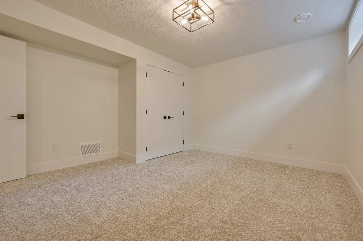 Empty room with beige carpet, white walls, a window, a small closet, and a modern ceiling light fixture.