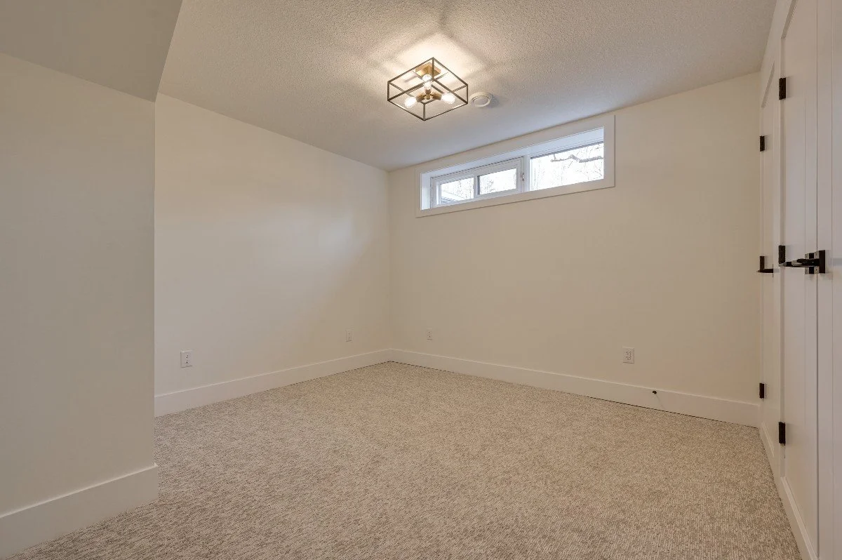 Empty room with white walls, beige carpet, a small horizontal window, and a ceiling light fixture.