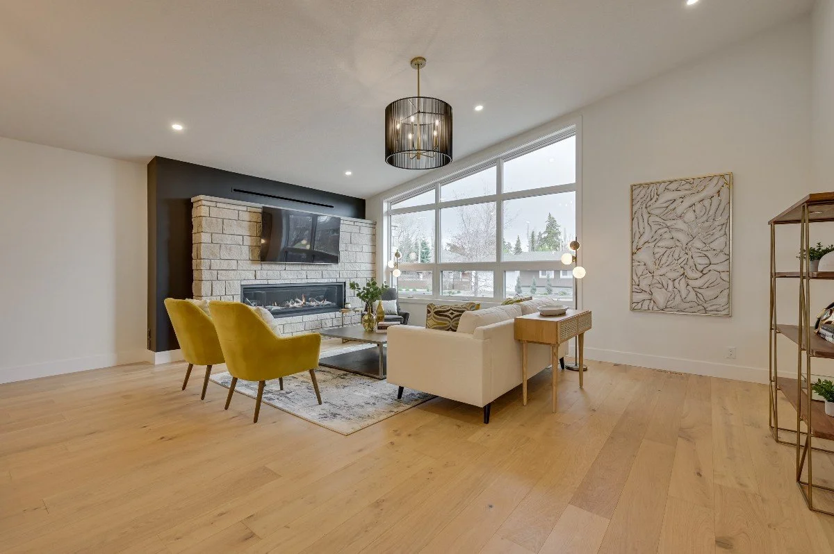 Modern living room with a stone fireplace, large window, white sofa, yellow accent chairs, and decorative items.