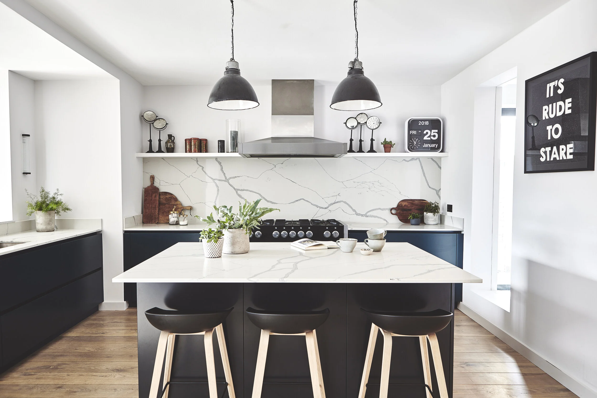 Blue kitchen cabinets and a marble splashback with industrial island lights and a range cooker. Open plan design by Stanza interior design, Balham