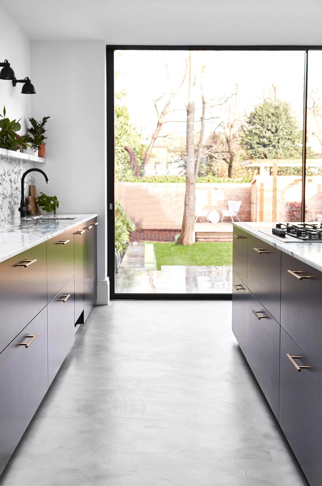 Poured concrete flooring with dark kitchen cabinets and marble worktop. Interior design of large family home in Balham,