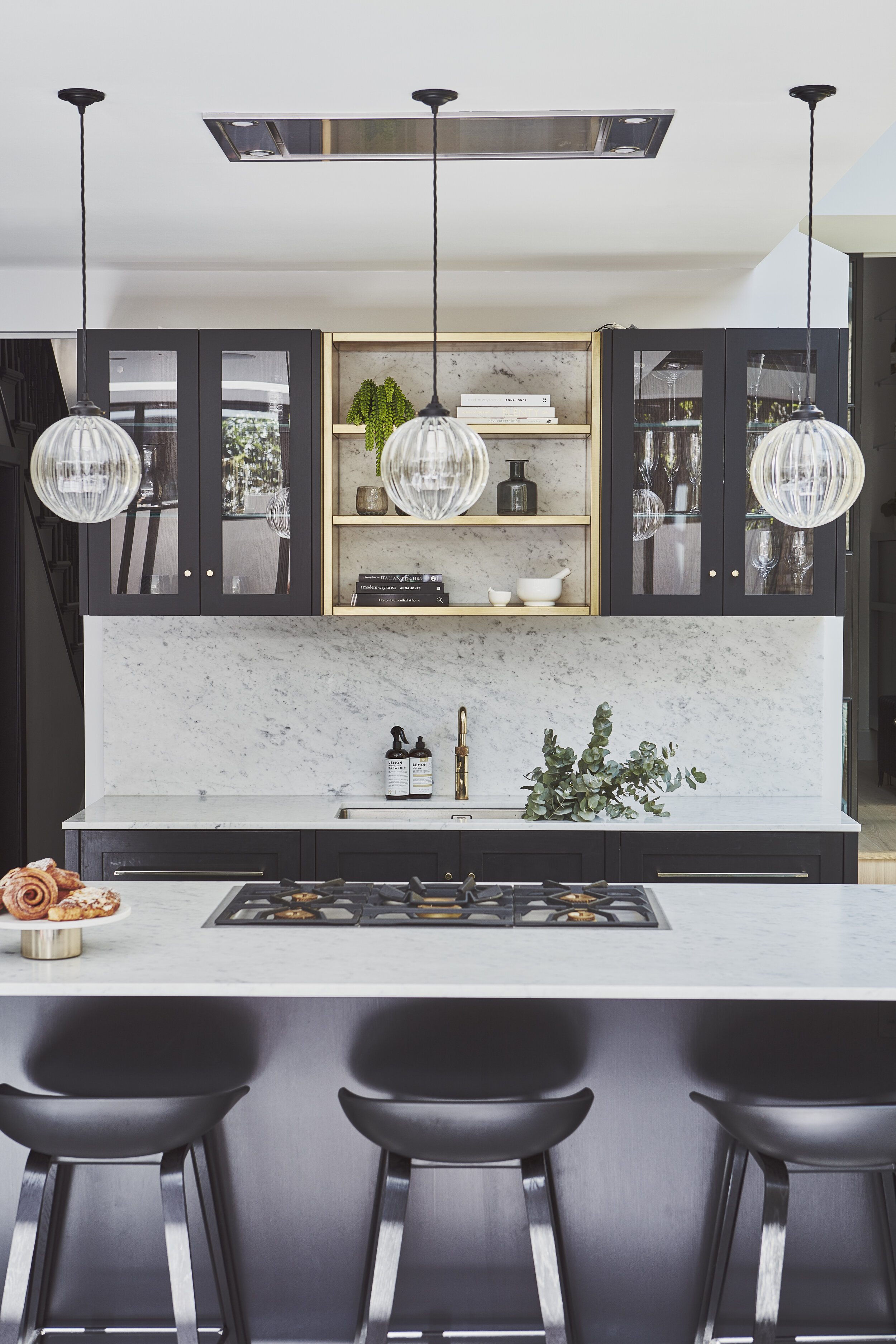 Dark kitchen design in Clapham Common. Dark cabinets with marble worktop, brass quooker, ribbed lights above island and recessed extractor. Kitchen design by Stanza interior design, Wandsworth