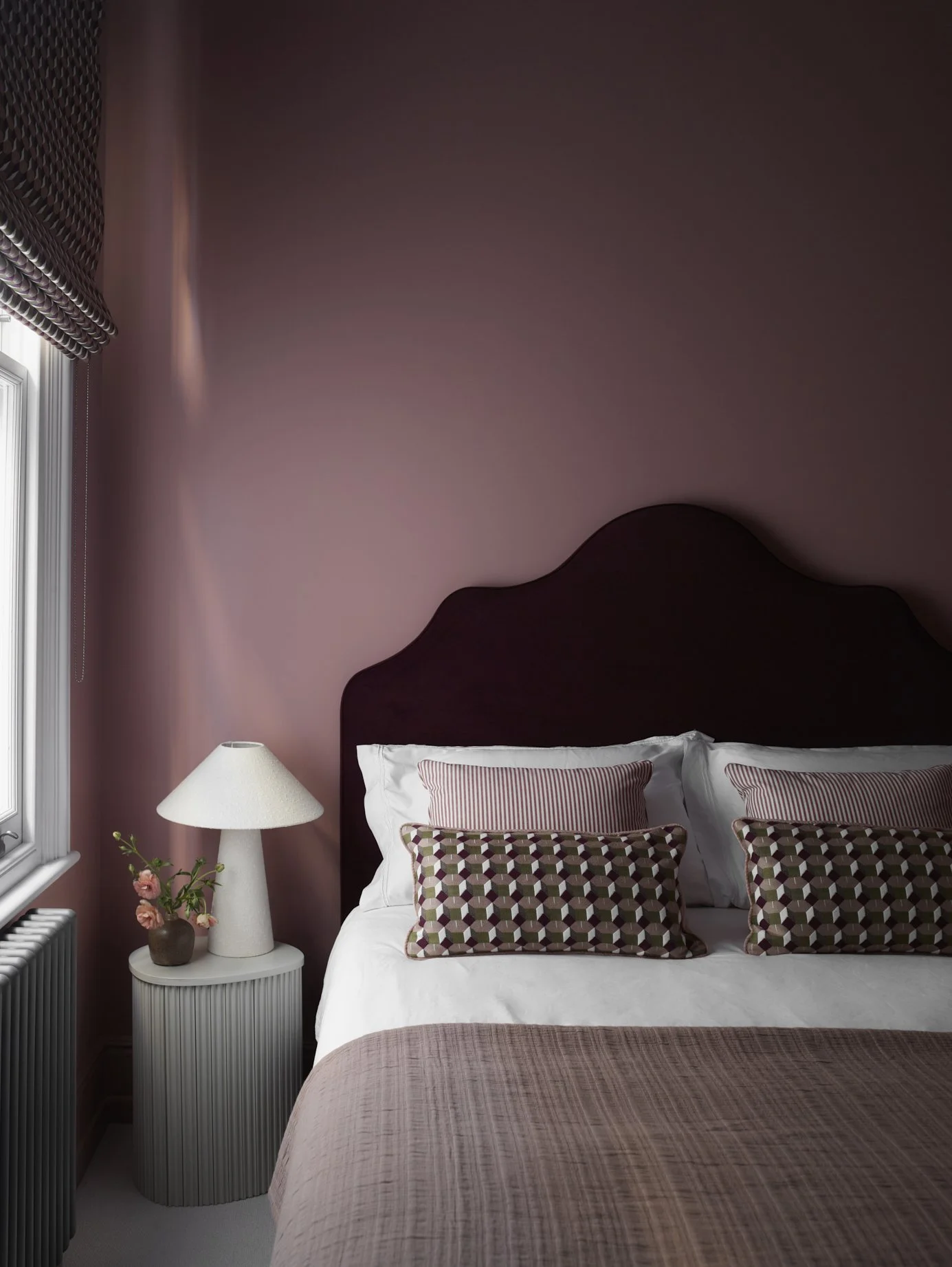 Deep pink bedroom design with bespoke upholstered headboard and tonal cushions. Interior design in Wandsworth