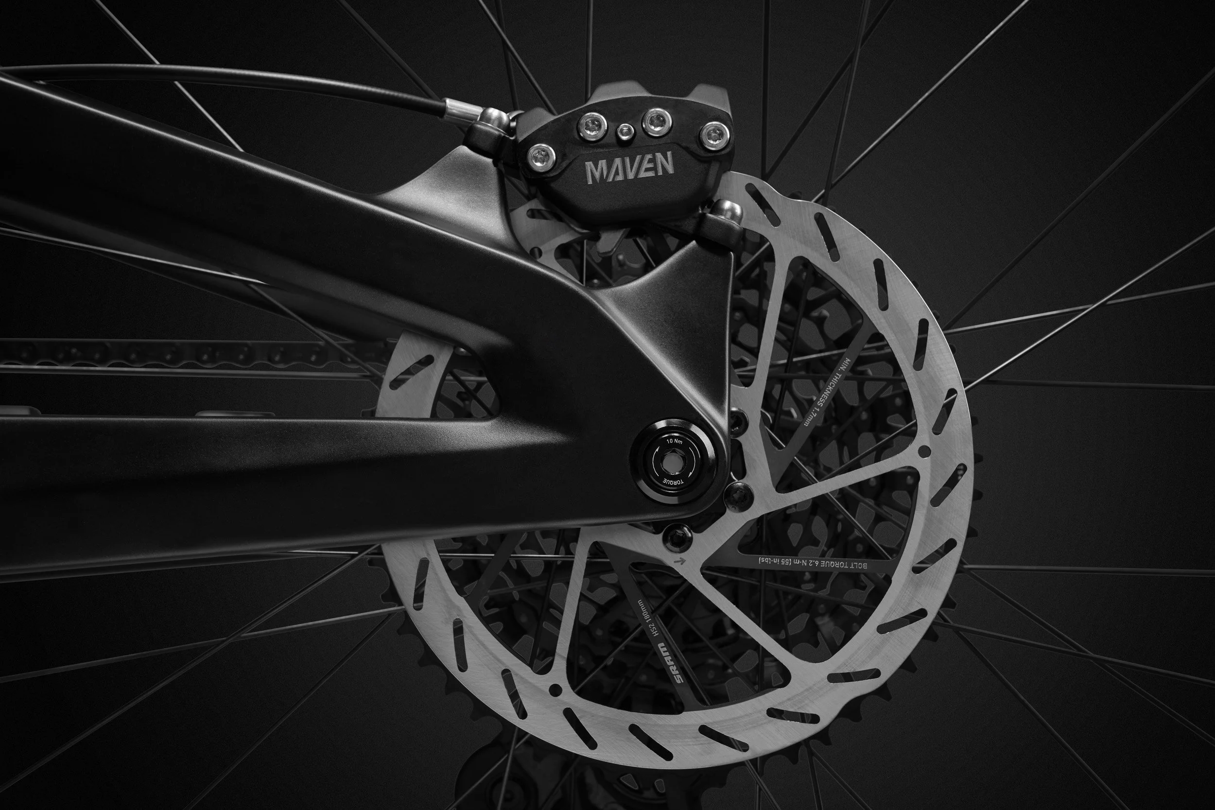 Close-up of a bicycle's disc brake and suspension system in black and white.