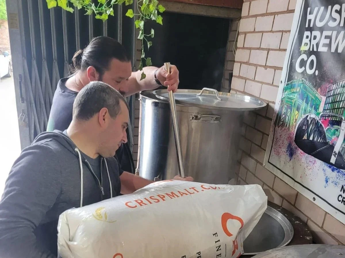 2 men pouring in malt while making beer